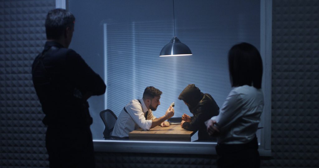 Medium shot of a male and a female police officer watching their colleague interrogating someone
