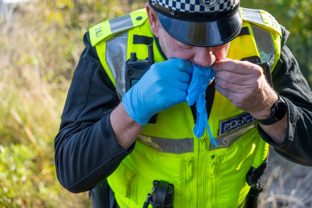Picture of a police officer blowing into a blue rubber glove in order to put it on easier 