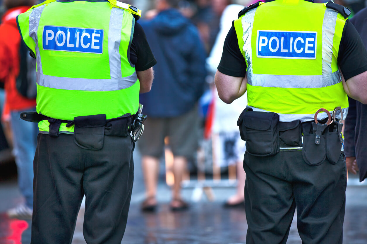 A picture of the back of two police officers stood on a busy street 