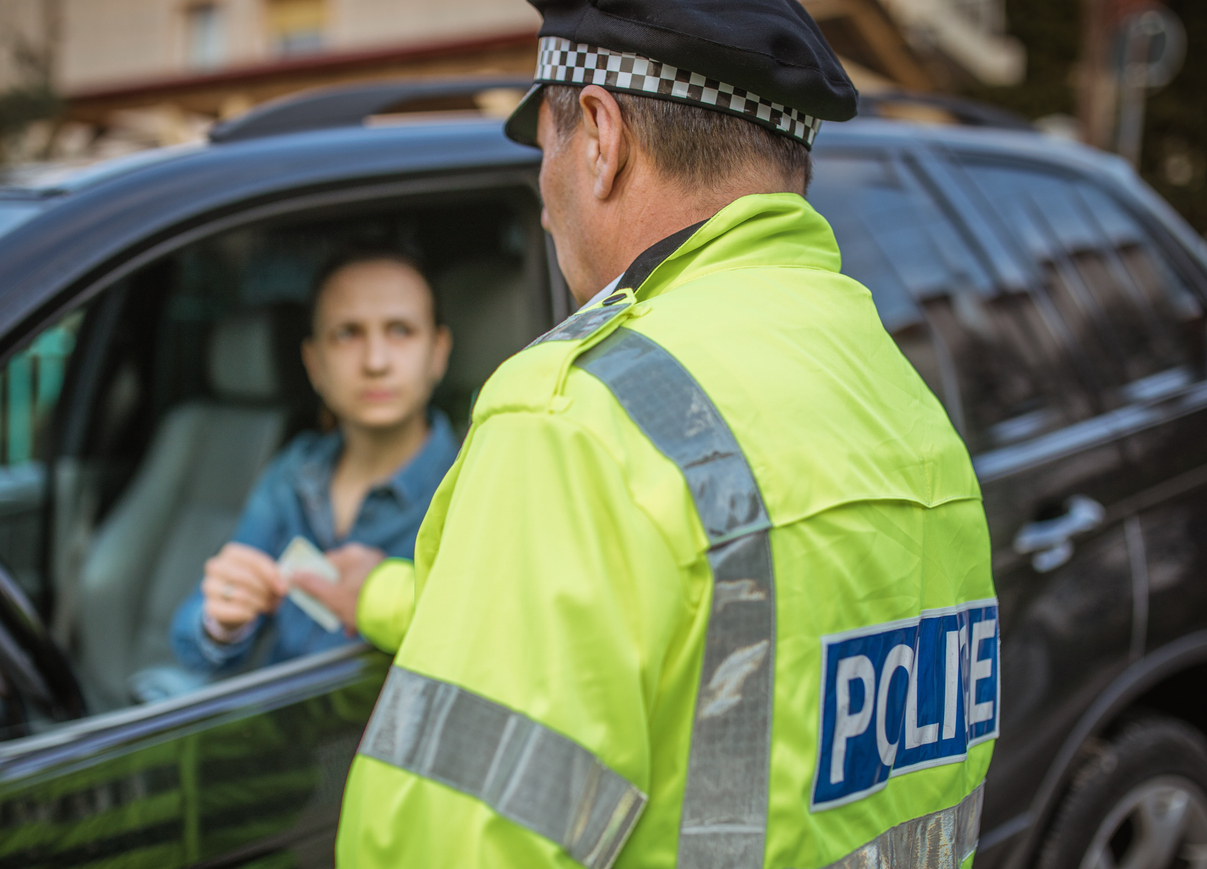 police officer making a traffic stop on the street, woman in the car handing the officer her license 
