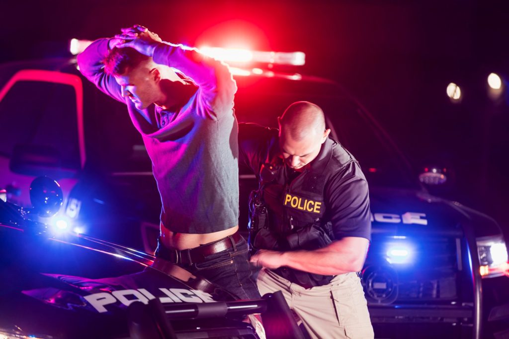 A police officer carrying out a search of a man next to a police car