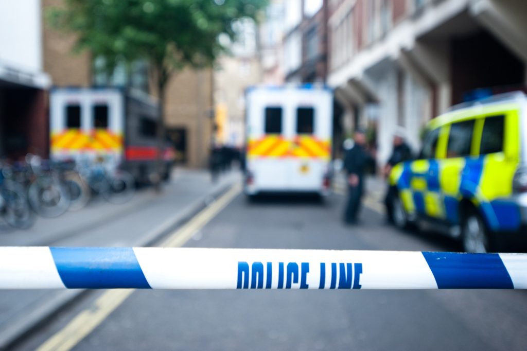 A strip of police tape in the foreground with blurred police vehicles in the background