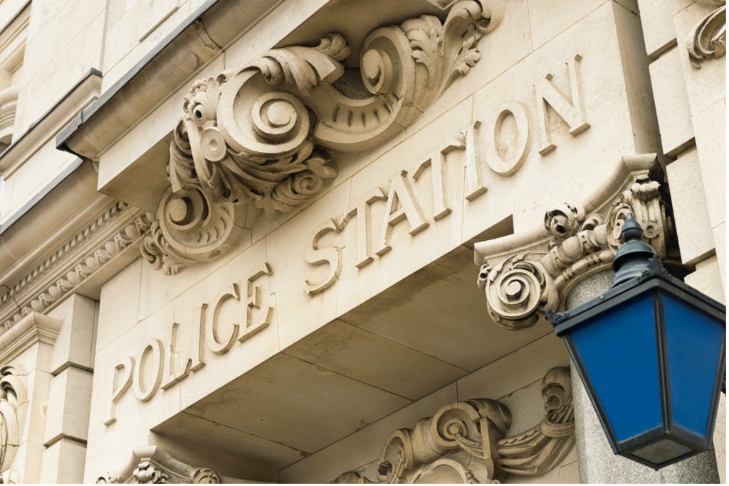 A picture of a police station, up close image of the words 'Police station' carved into a stone building above a doorway 