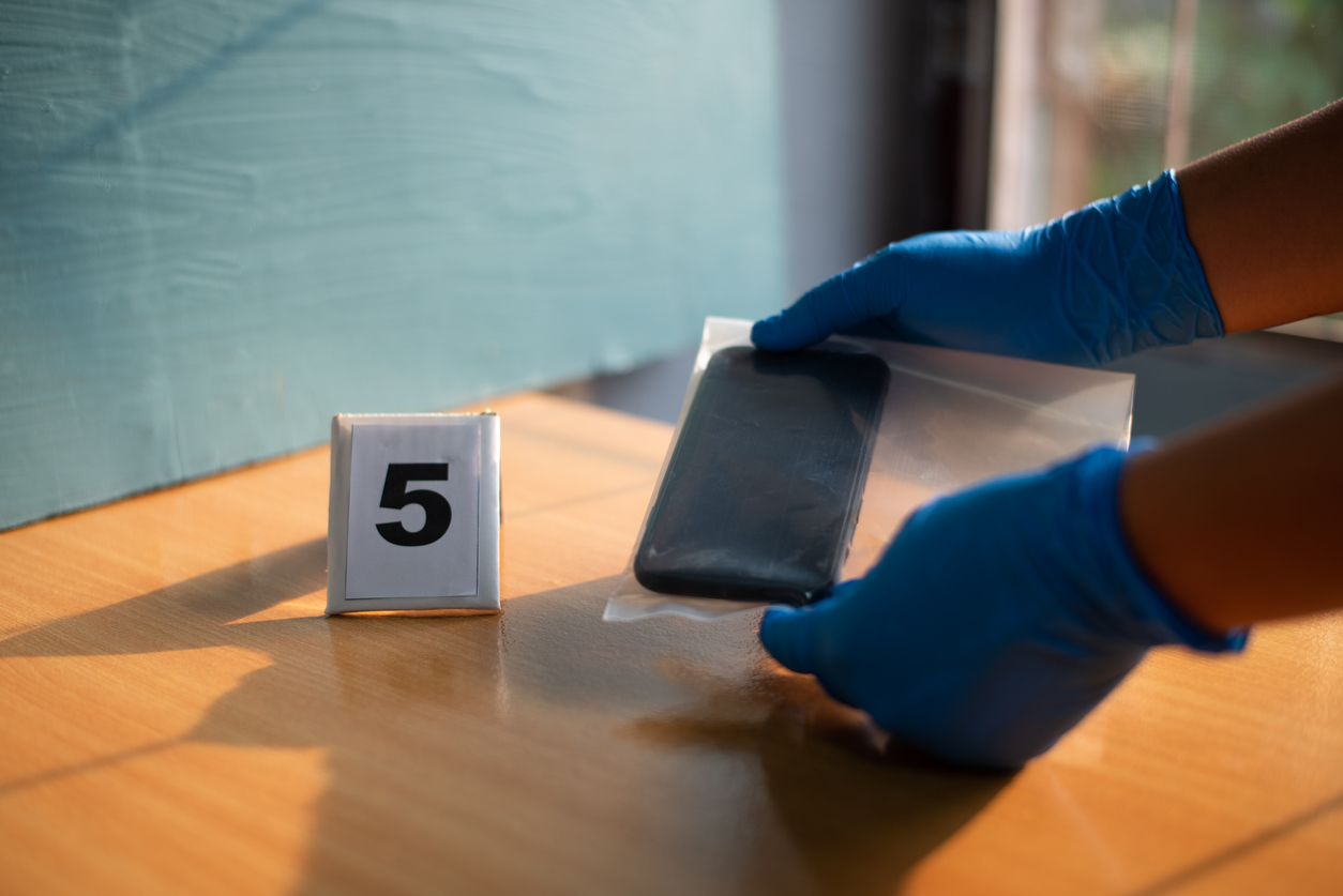 Hand scientist in blue glove holding an evidence bag with a phone in 