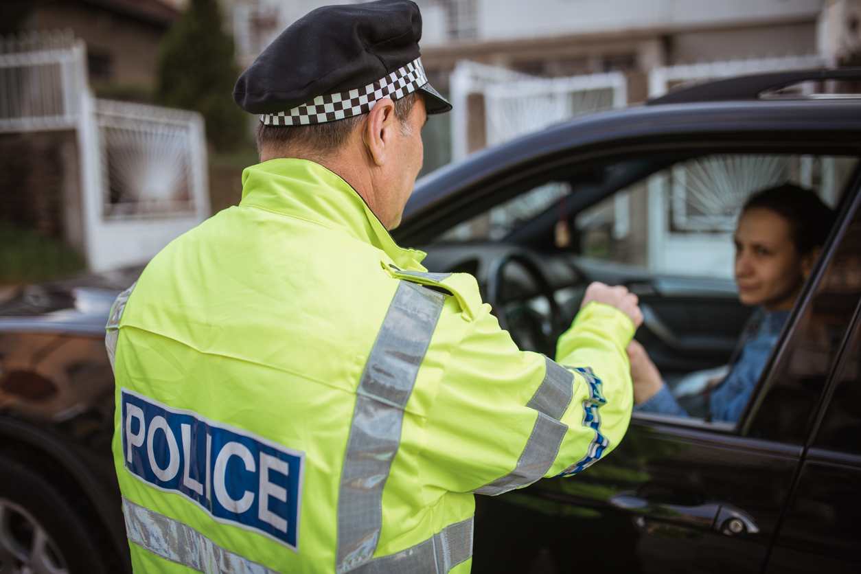 Young woman pulled over by police officer on the road, the police officer wearing a high visibility jacket is talking to the woman through the window.