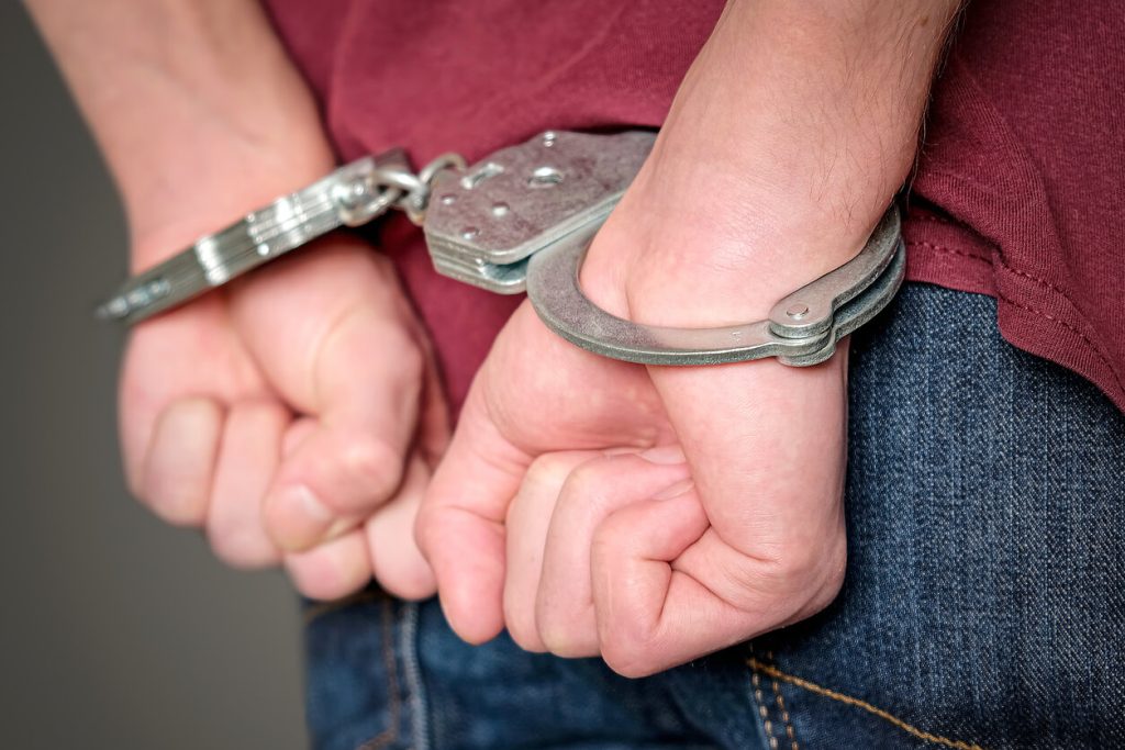 A person making fists with both their hands while handcuffed behind their back