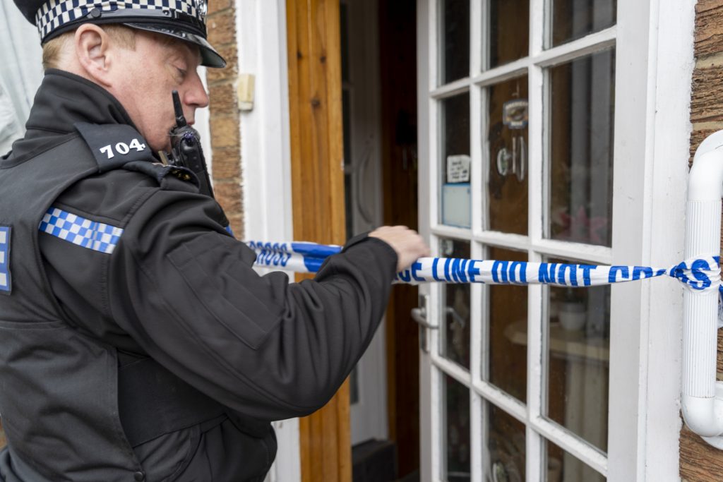 A policeman putting barricade tape across an elderly person's doorway.