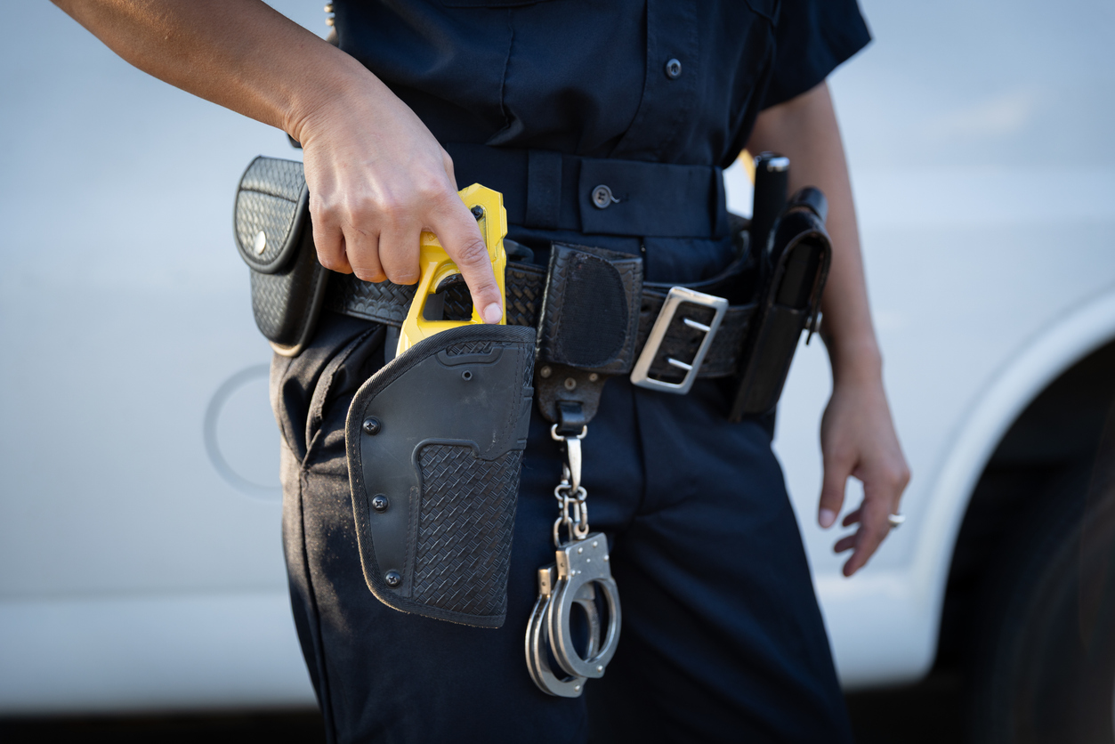 Image of a police officer with a taser in their belt and their holding it as if to draw it. 
